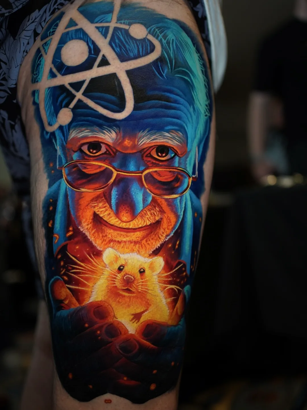 Tattoo of an elderly man holding a glowing mouse, with an atom symbol above his head.