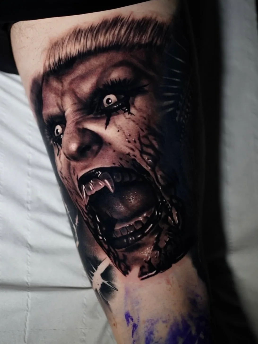 Realistic vampire face tattoo on upper arm with open mouth and sharp teeth.