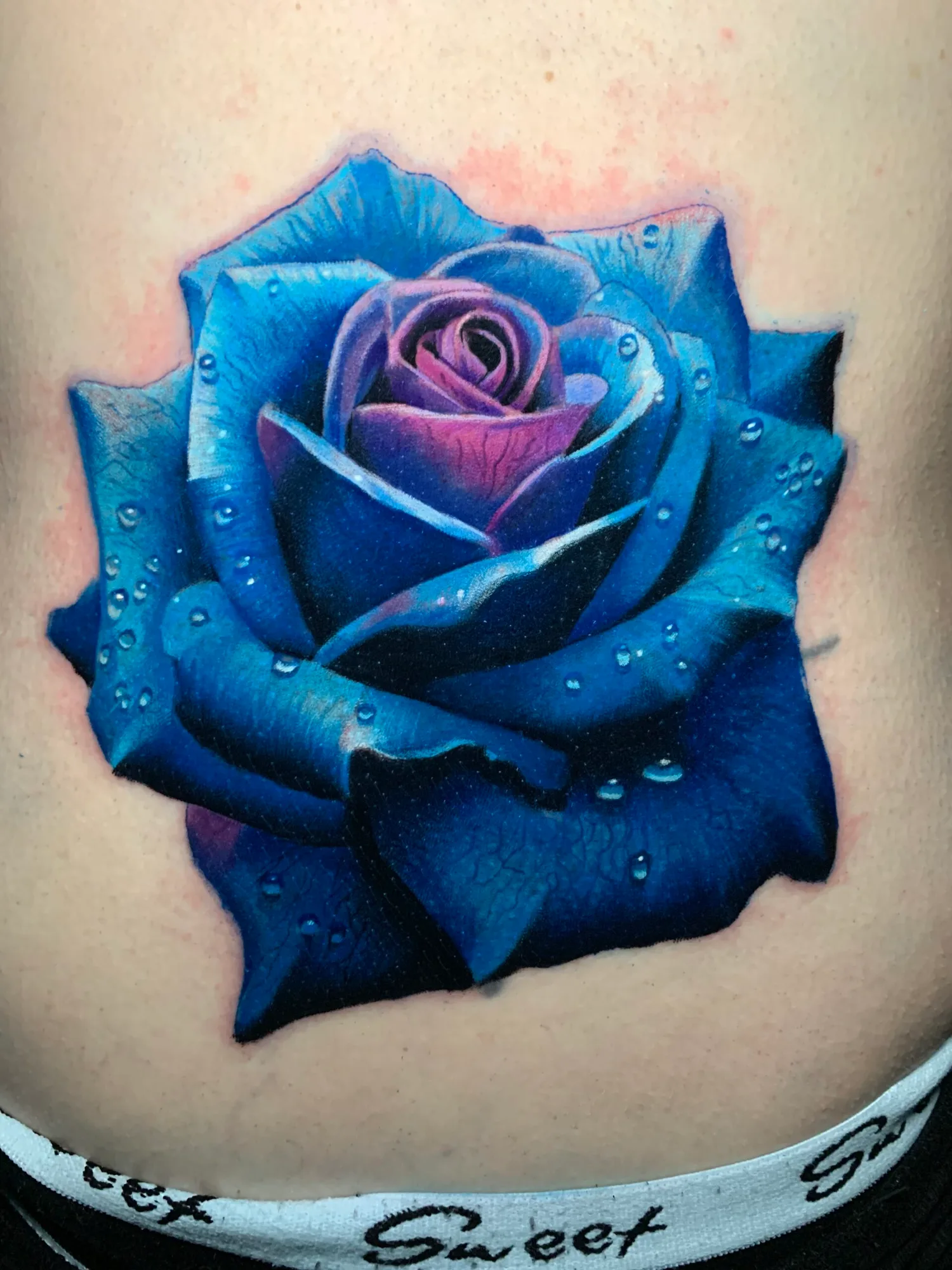 Realistic tattoo of a blue rose with water droplets.