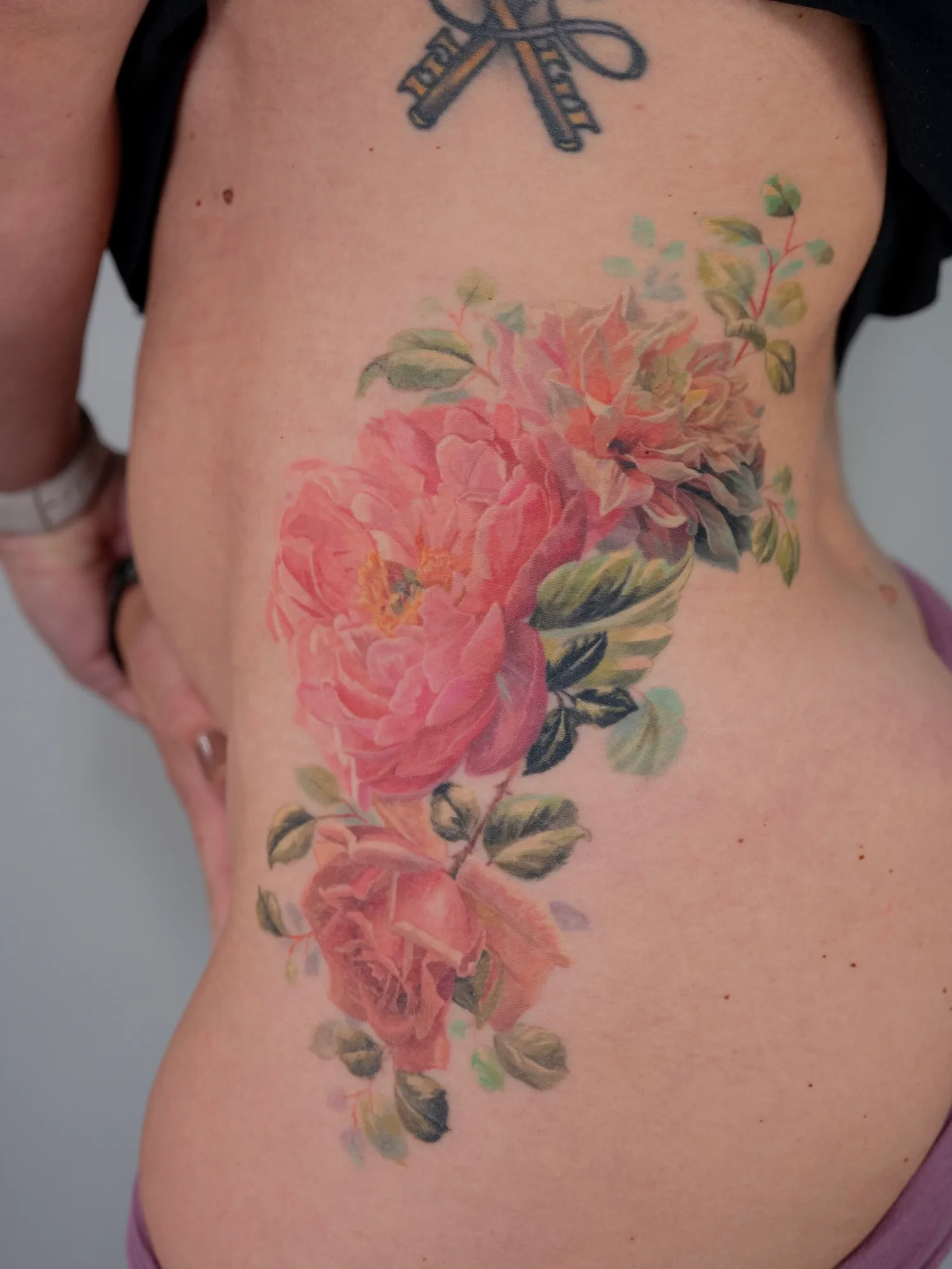 Realistic floral tattoo with pink roses and peonies on upper hip.