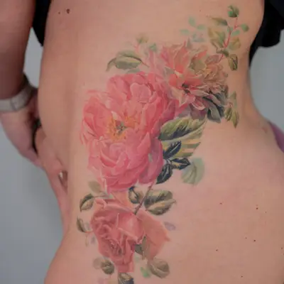 Realistic floral tattoo with pink roses on upper hip.