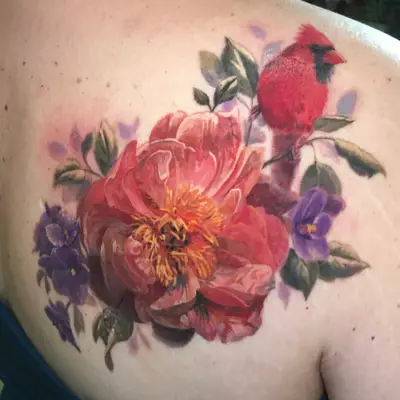 Colorful tattoo of a red cardinal with flowers on shoulder blade.