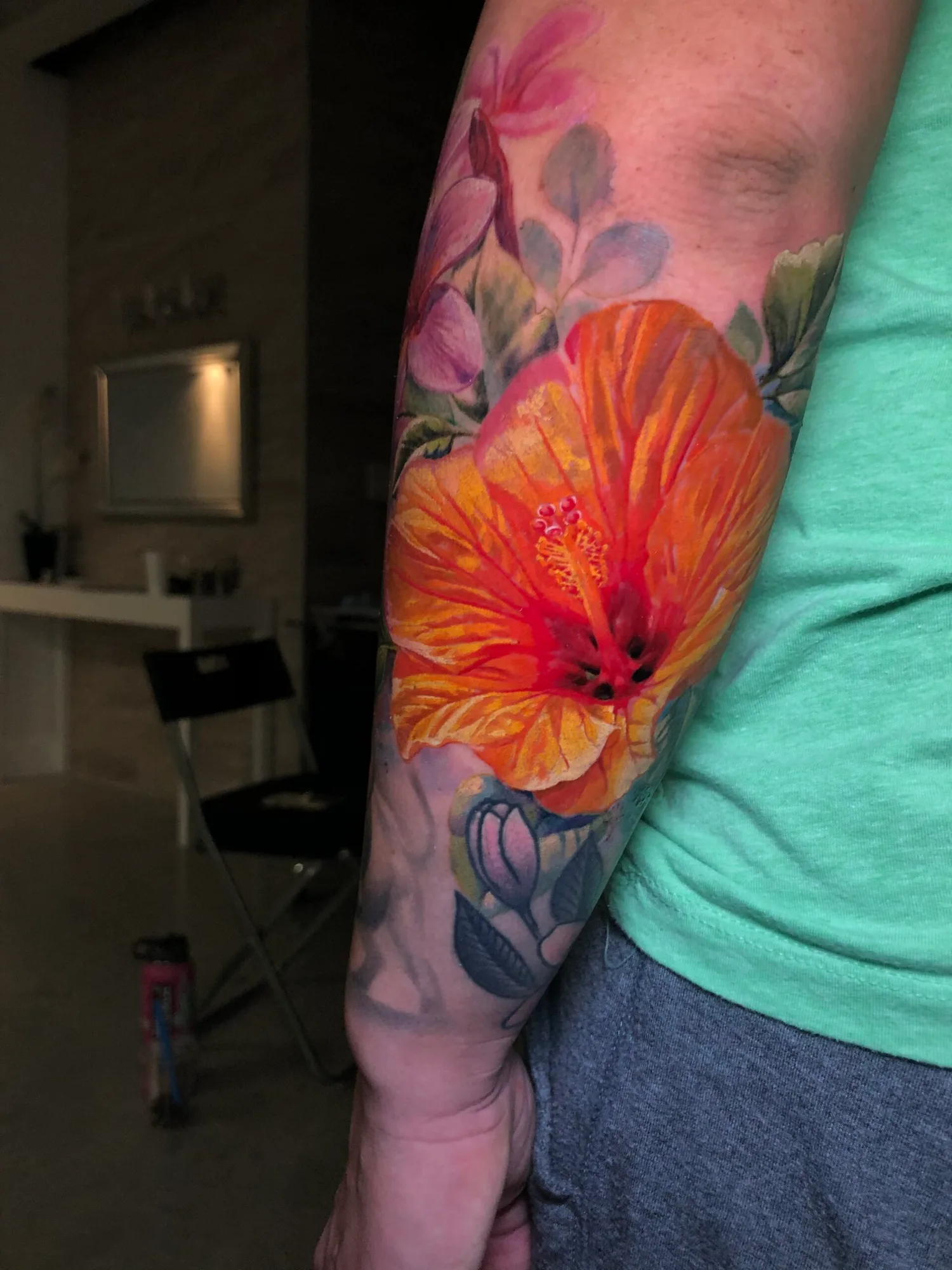 Colorful floral tattoo with a large orange hibiscus on arm.