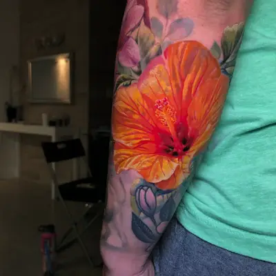 Colorful floral tattoo with a large orange hibiscus on arm.
