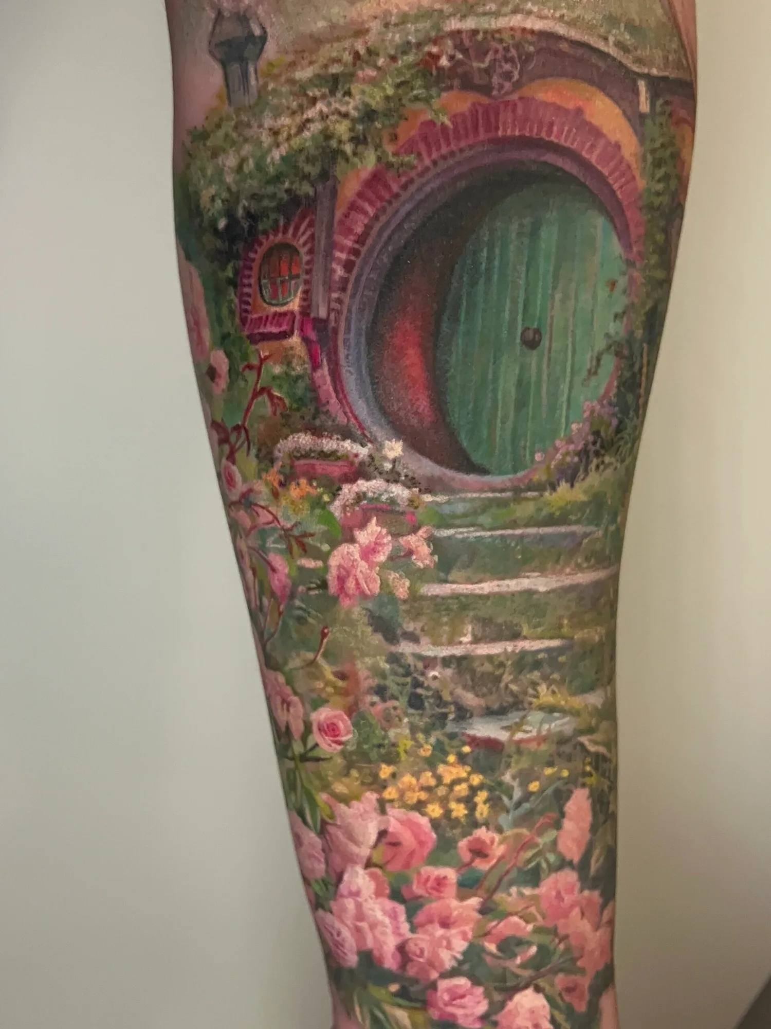 Tattoo of a hobbit door surrounded by flowers and greenery.