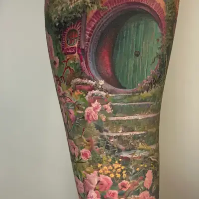 Tattoo of a hobbit door surrounded by flowers and greenery.