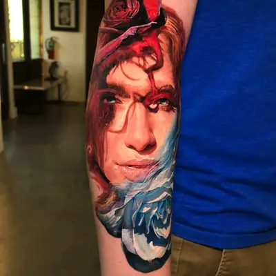 Tattoo of an expressive face with a rose overlay on forearm.
