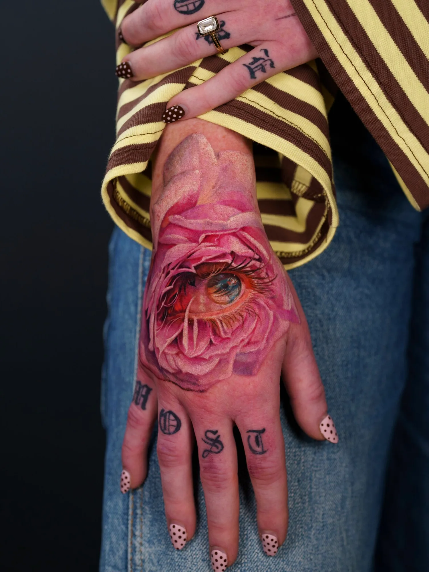Tattoo of a realistic eye within a pink rose on hand