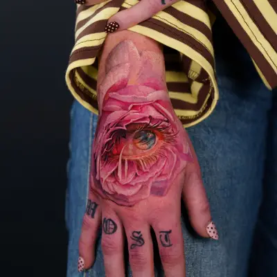 Tattoo of a realistic eye within a pink rose on hand