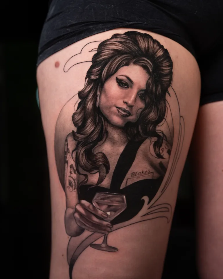 Black and grey tattoo of a woman holding a cocktail glass on a thigh.