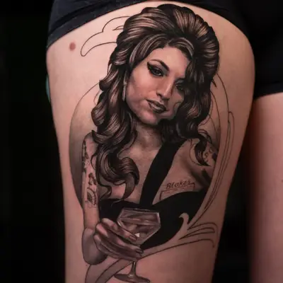 Black and grey tattoo of a woman holding a cocktail glass on a thigh.