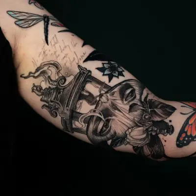 An arm tattoo featuring a realistic elephant and dragonfly, with intricate details and text.