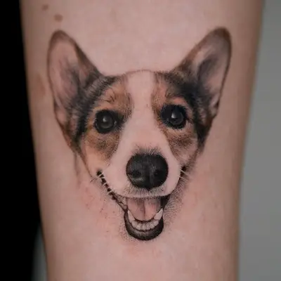 Realistic tattoo of a smiling Corgi dog's face on skin.