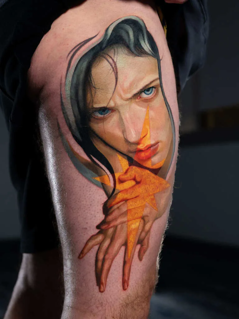 Surreal tattoo of a woman's face with geometric shapes on thigh.