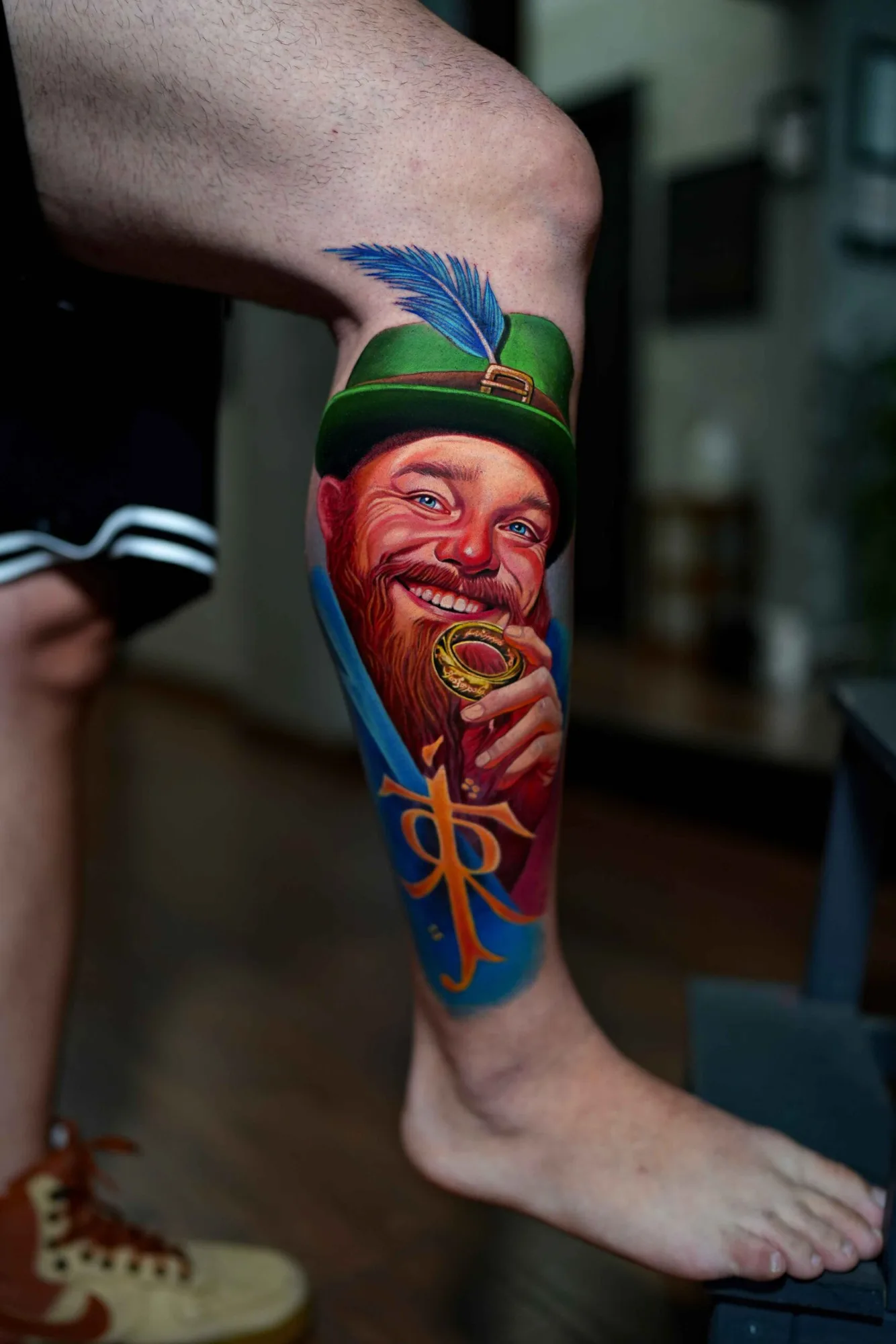 Tattoo of a cheerful man with a beard and green hat holding a ring.
