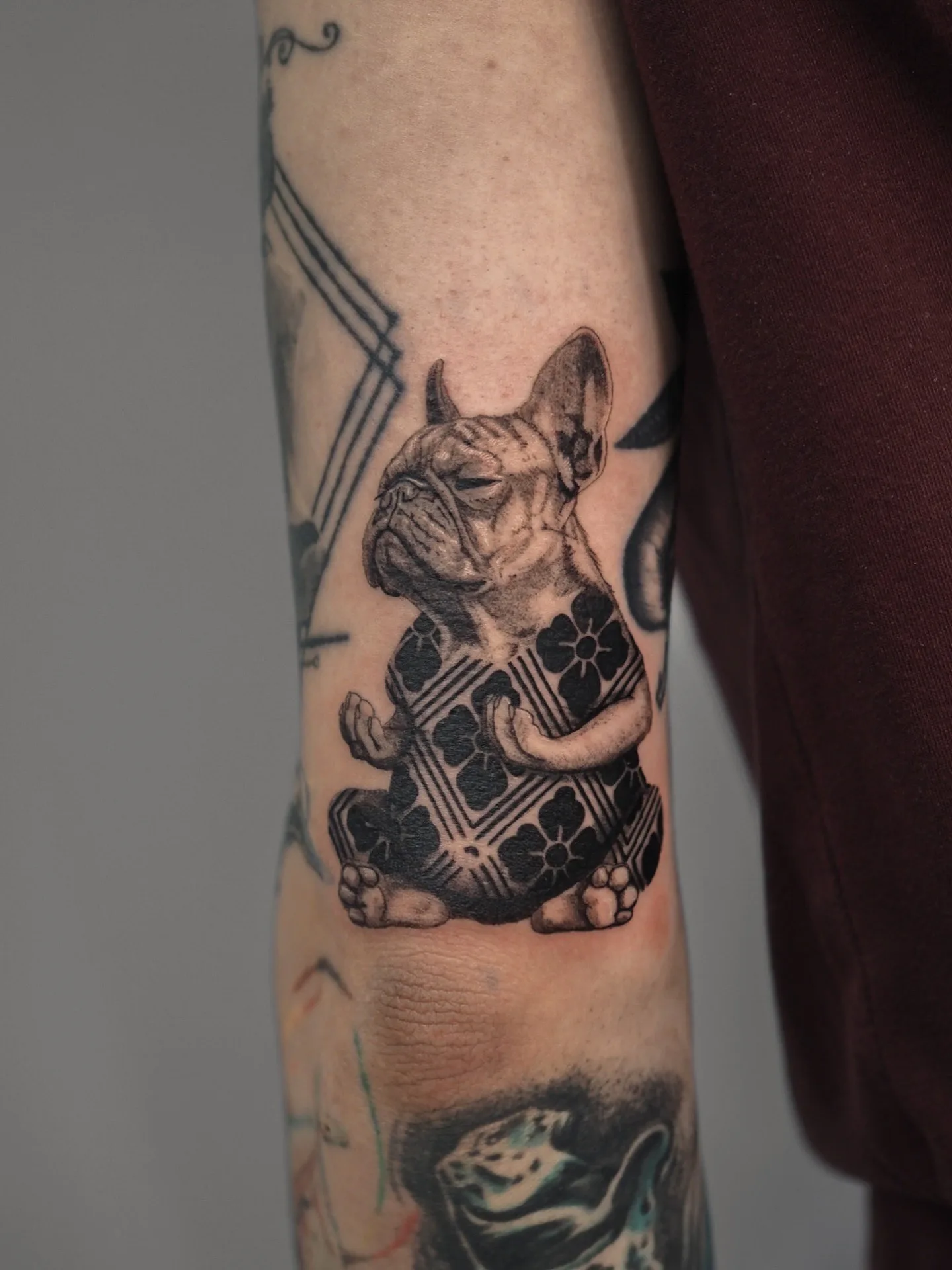 Tattoo of a meditating bulldog in a patterned outfit on upper arm.