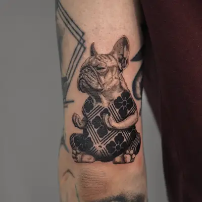 Tattoo of a meditating bulldog in a patterned outfit on upper arm.