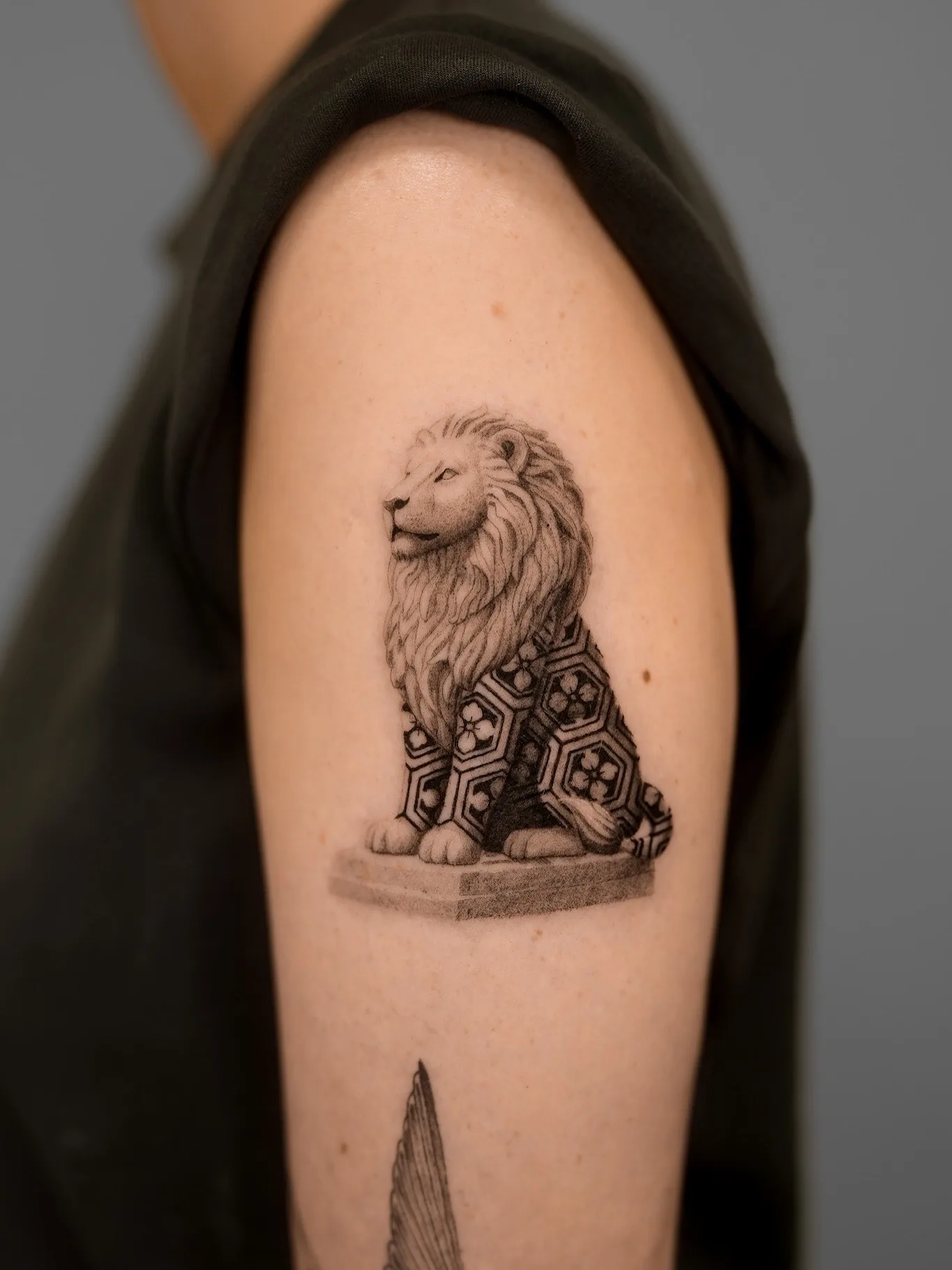 Tattoo of a lion with geometric patterns on upper arm.