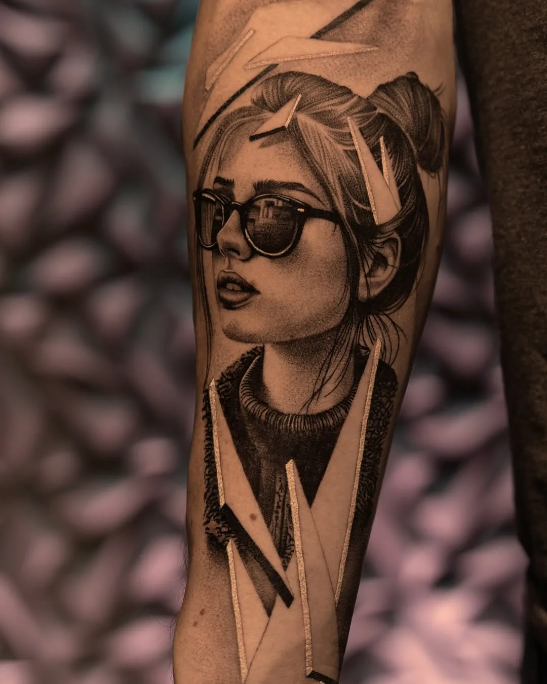 Black and grey tattoo of a woman with sunglasses on an arm.