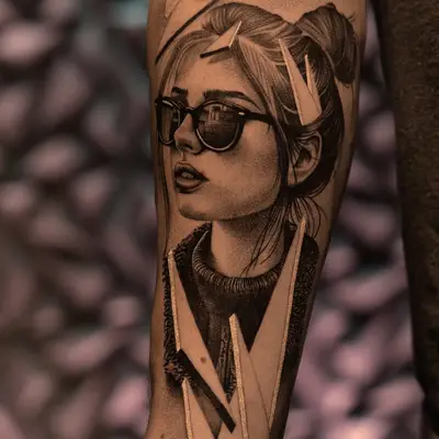 Black and grey tattoo of a woman with sunglasses on an arm.