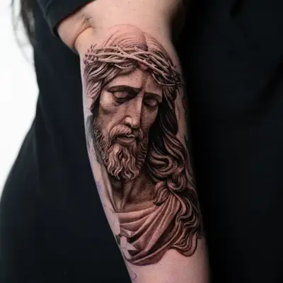 Tattoo of Jesus with crown of thorns in black and grey on upper arm.
