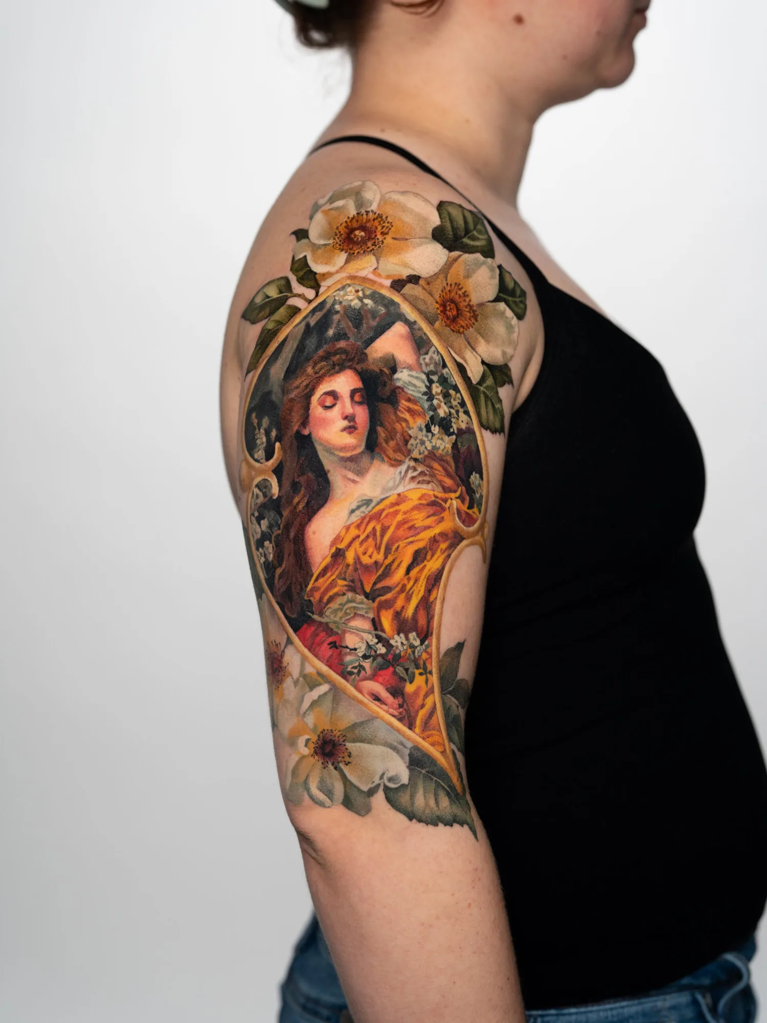 Colorful art nouveau style tattoo on upper arm with flowers and a woman.