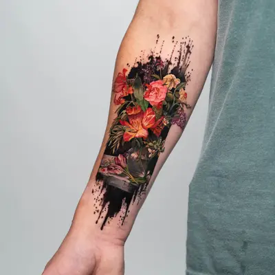 Forearm tattoo of colorful flowers with black ink splashes.