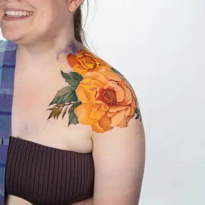 Colorful floral tattoo on woman's shoulder depicting orange roses.