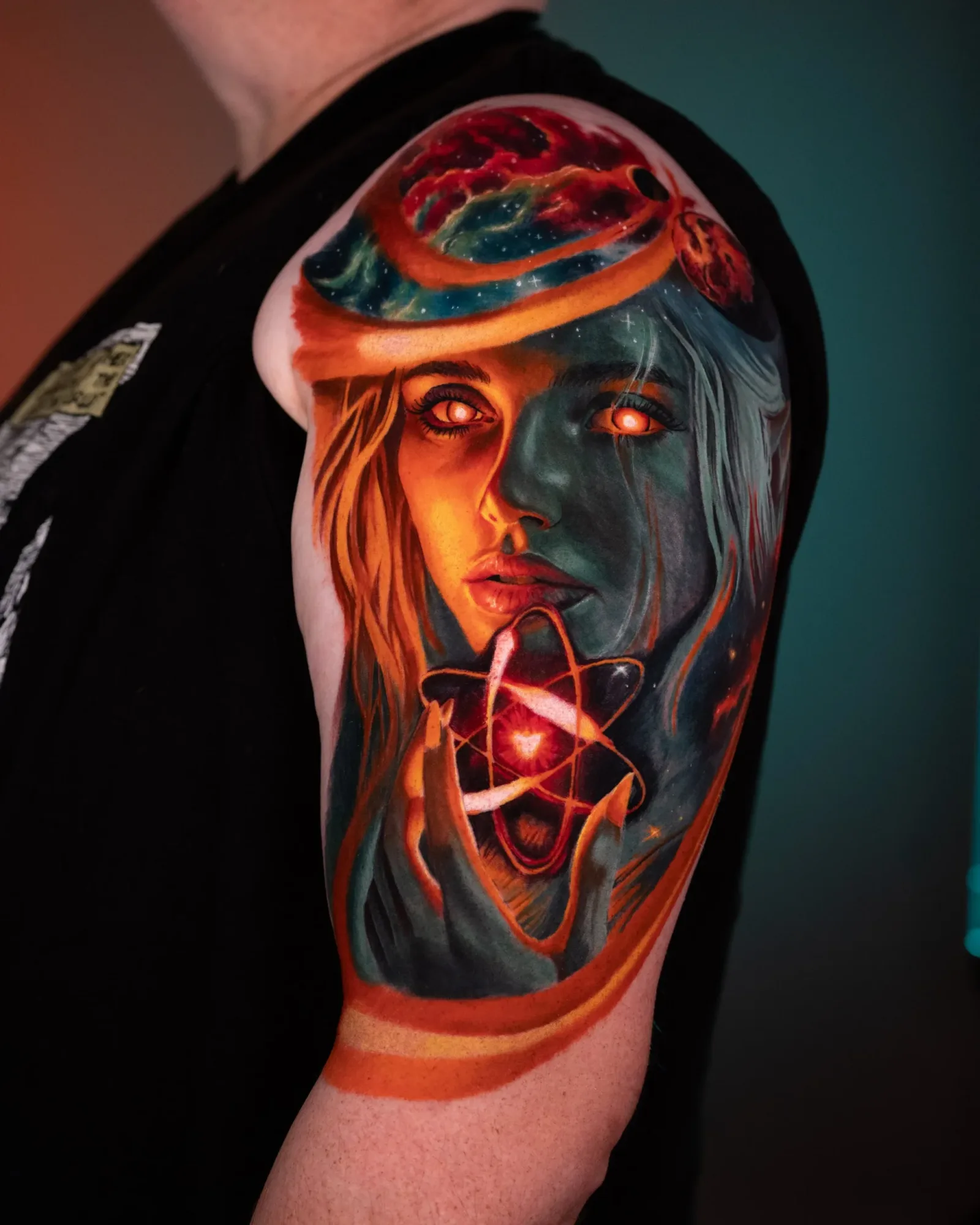 Colorful tattoo of a woman's face with cosmic elements on upper arm.