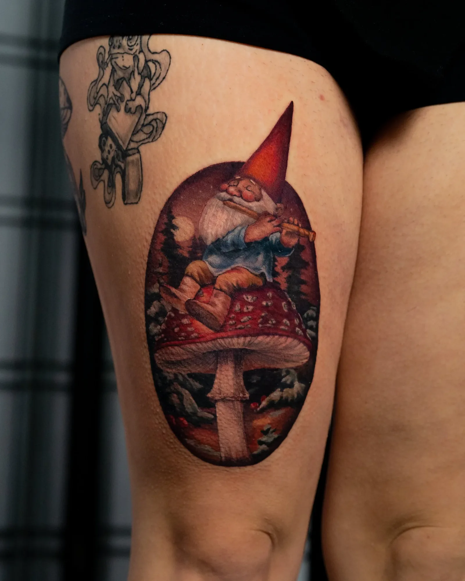 Tattoo of a gnome sitting on a mushroom on a person's upper thigh.