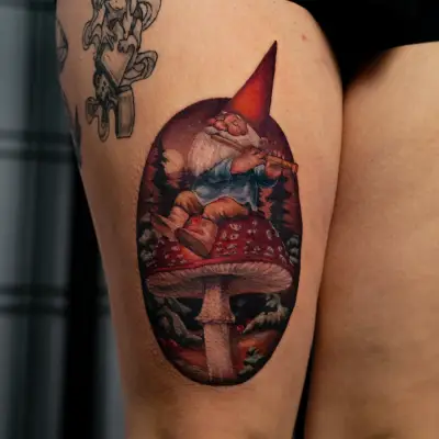 Tattoo of a gnome sitting on a mushroom on a person's upper thigh.