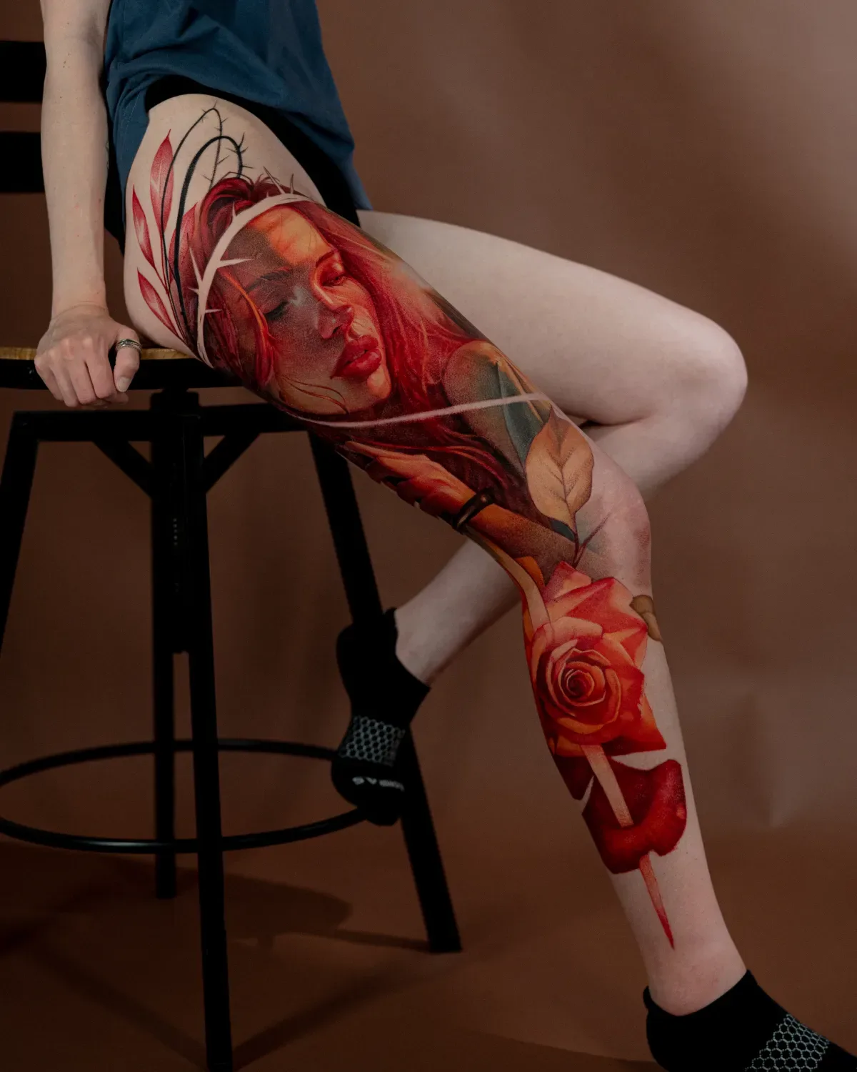 Tattoo of a woman's face with red hair and a rose on the leg.