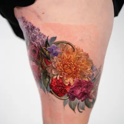 Color realism tattoo of lilacs, a wood violet, an orange chrysanthemum, a red carnation and a magenta rhododendron with gold scrollwork, on an outer right thigh.