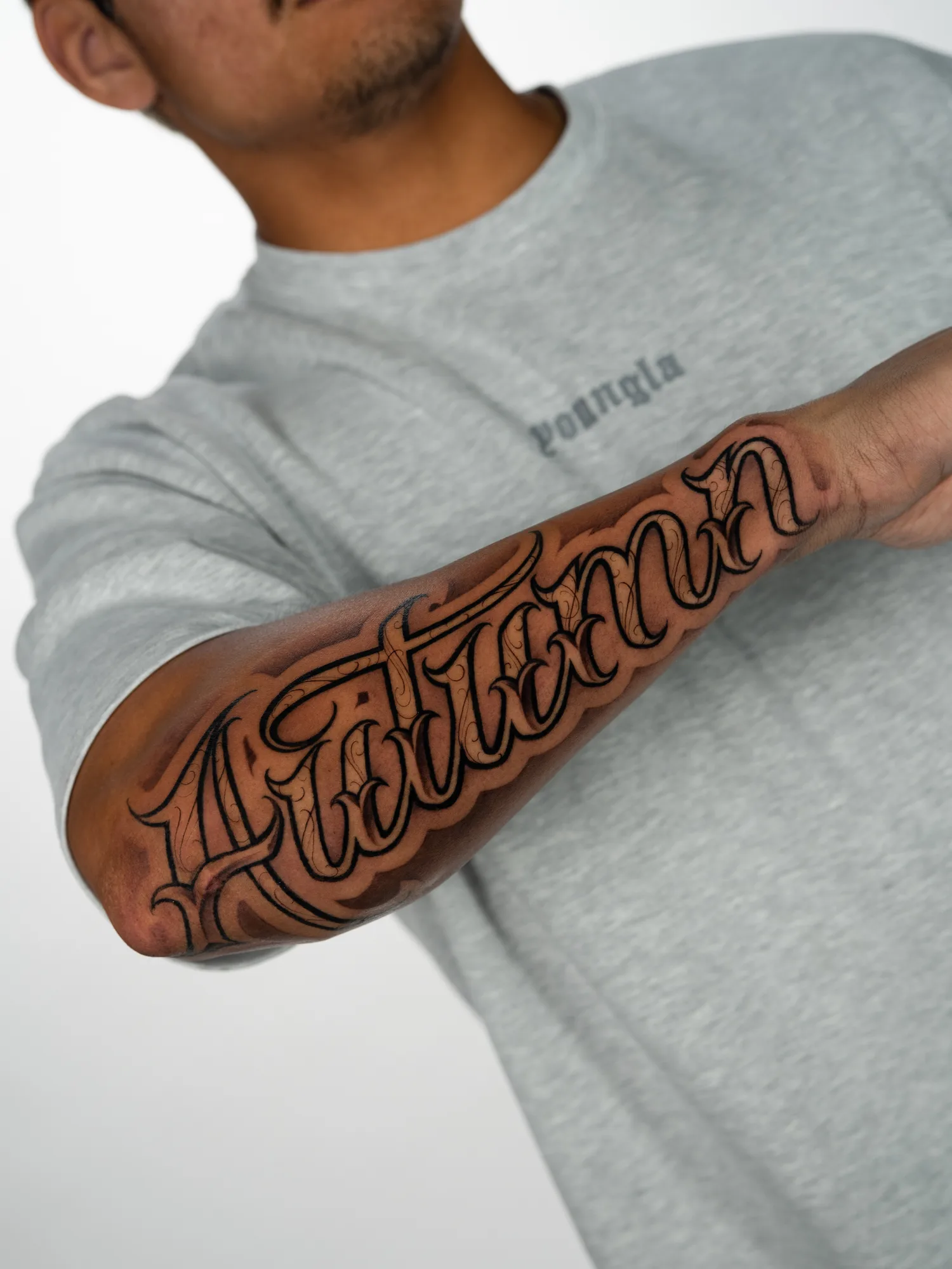 Black and grey tattoo of the name Autumn in ornate script with fine filigree, running from elbow to wrist along an outer forearm.
