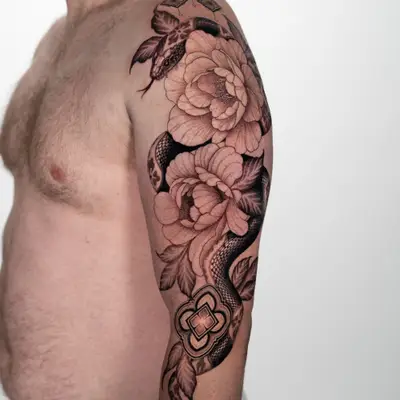Black and grey half sleeve of a snake winding through two large peonies across a shoulder and upper arm, with ornamental medallions near the elbow.