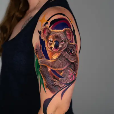 Full color realism tattoo of a mother koala with a joey on her back, holding a eucalyptus branch, against a purple and black graphic background on an upper arm.