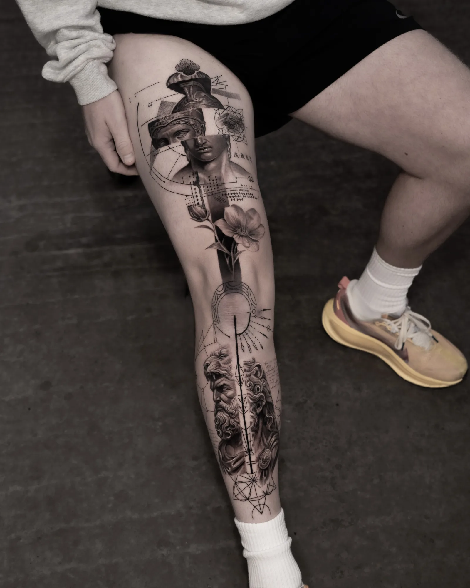 Black and grey leg tattoo running thigh to ankle with a veiled classical bust, a flower, a bearded god bust and sacred geometry.