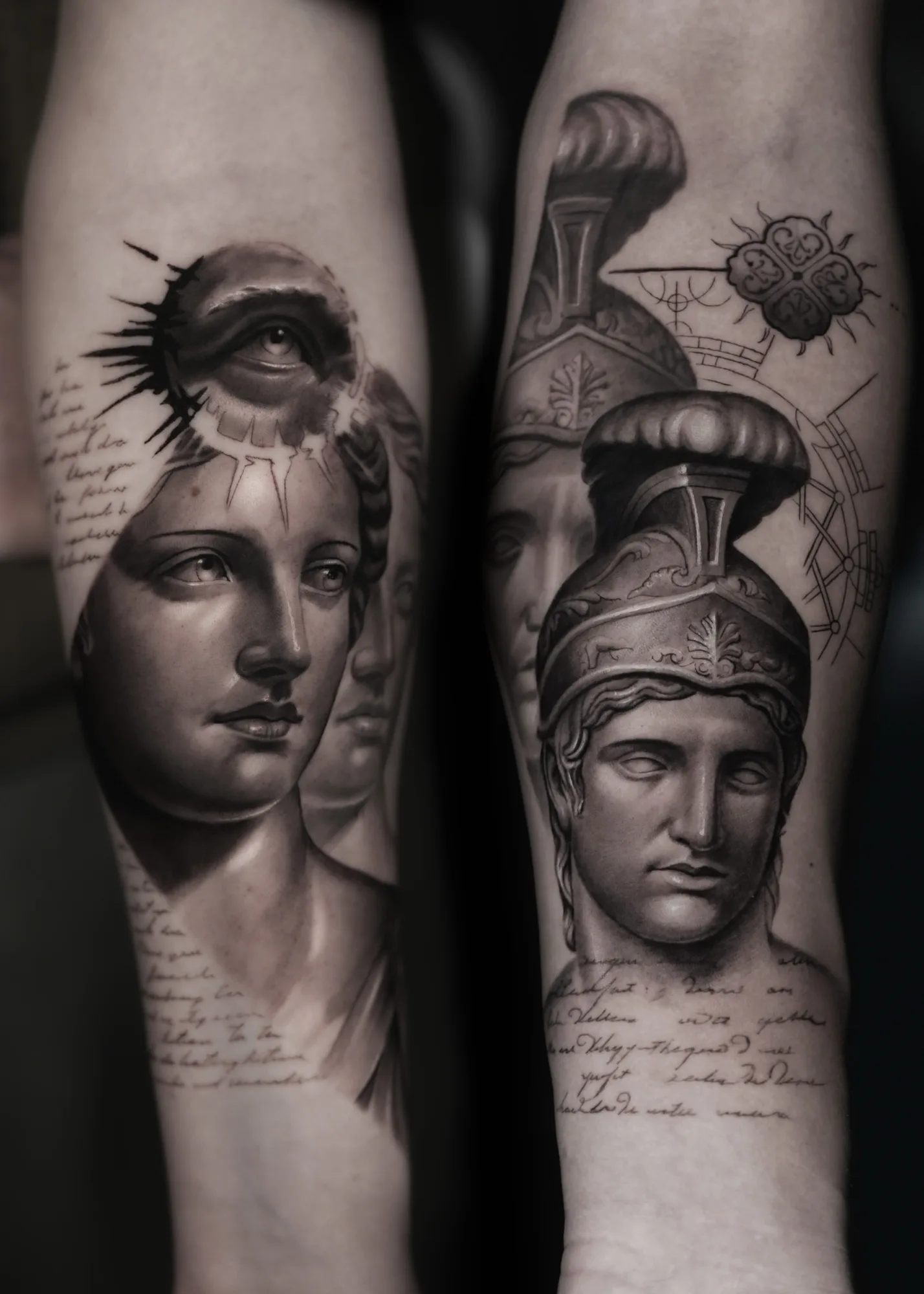 Two black and grey forearm tattoos photographed together, one a female classical bust with an eye set into the forehead, the other a helmeted warrior bust with an ornamental rosette and architectural line work.