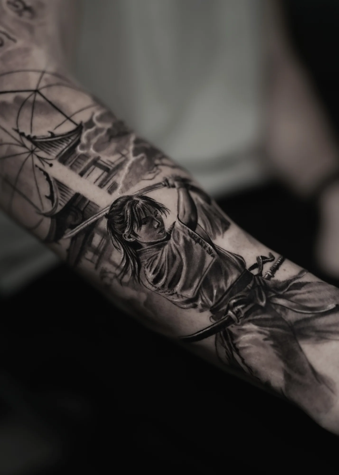 Black and grey forearm tattoo of a samurai mid-swing with a katana, a pagoda and clouds behind.