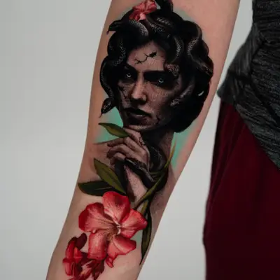 Medusa portrait on an inner forearm with snakes coiling from her hair, the face cracked like marble, worked in black and grey with red oleander flowers and a teal background in full color.