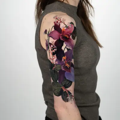 Color realism tattoo of purple and magenta jewel orchids with dark veined leaves, running down an upper arm.