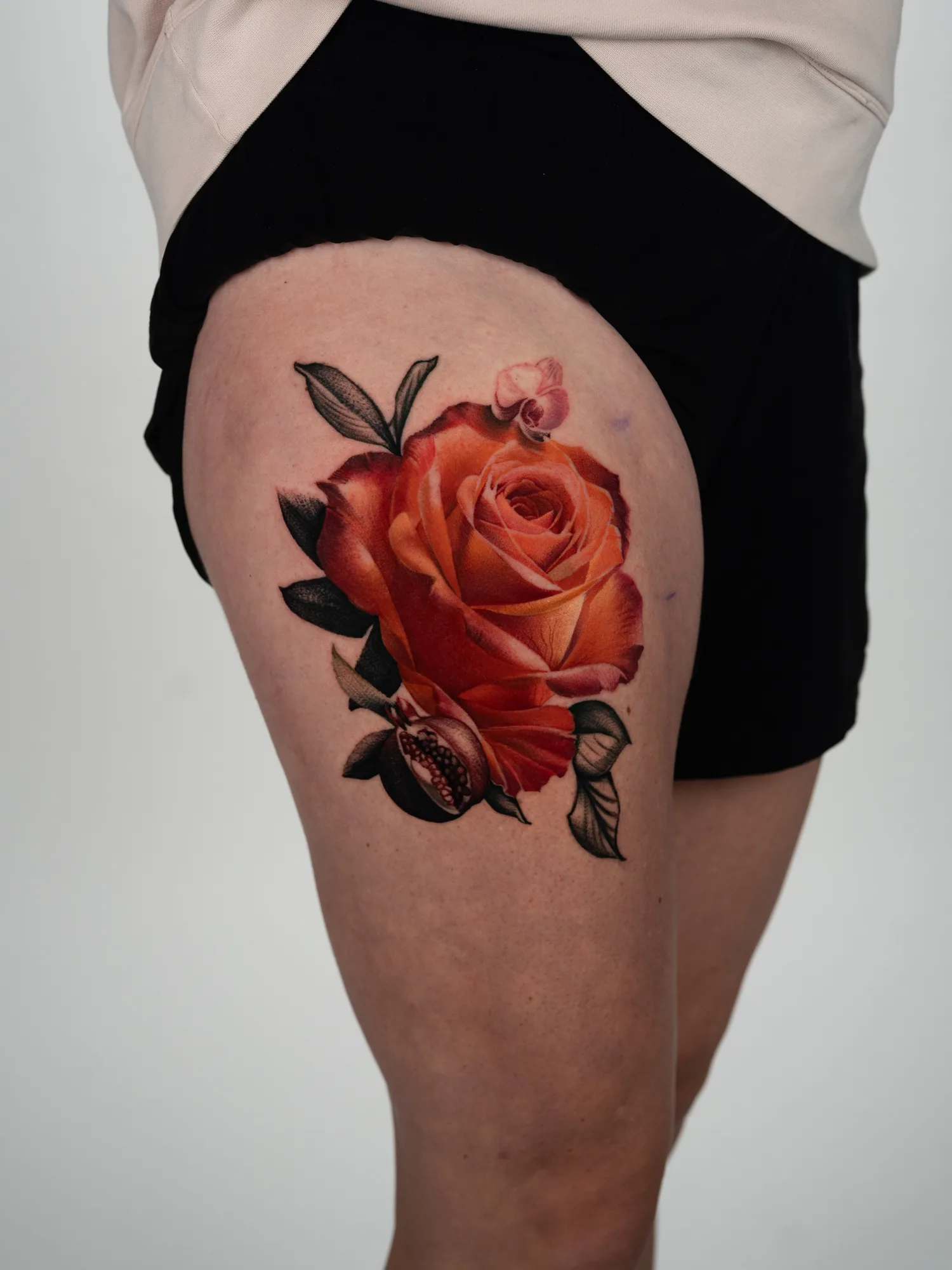 Large orange rose with a split pomegranate and an orchid bud on a thigh, blooms in full color and the leaves in black and grey.