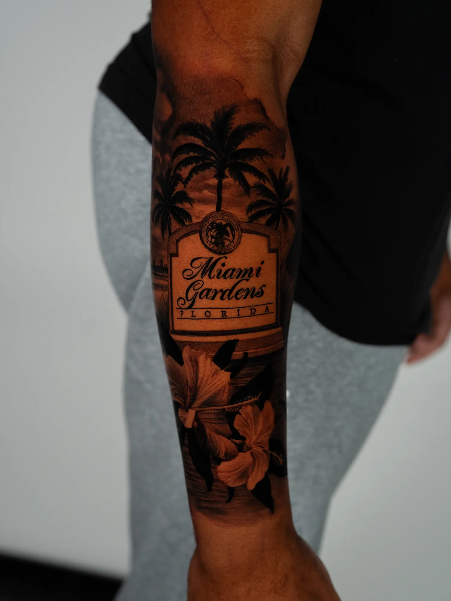 Miami Gardens Florida city sign with its municipal seal, framed by palm trees and hibiscus flowers, wrapping a forearm in black and grey.