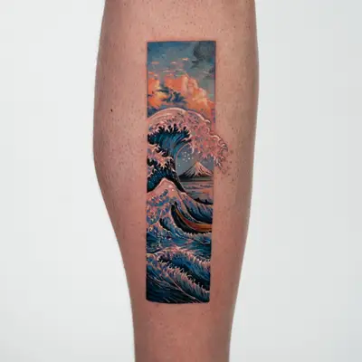 Hokusai's Great Wave with Mount Fuji behind it, tattooed in a vertical frame on the side of a calf, with foam breaking out past the border.