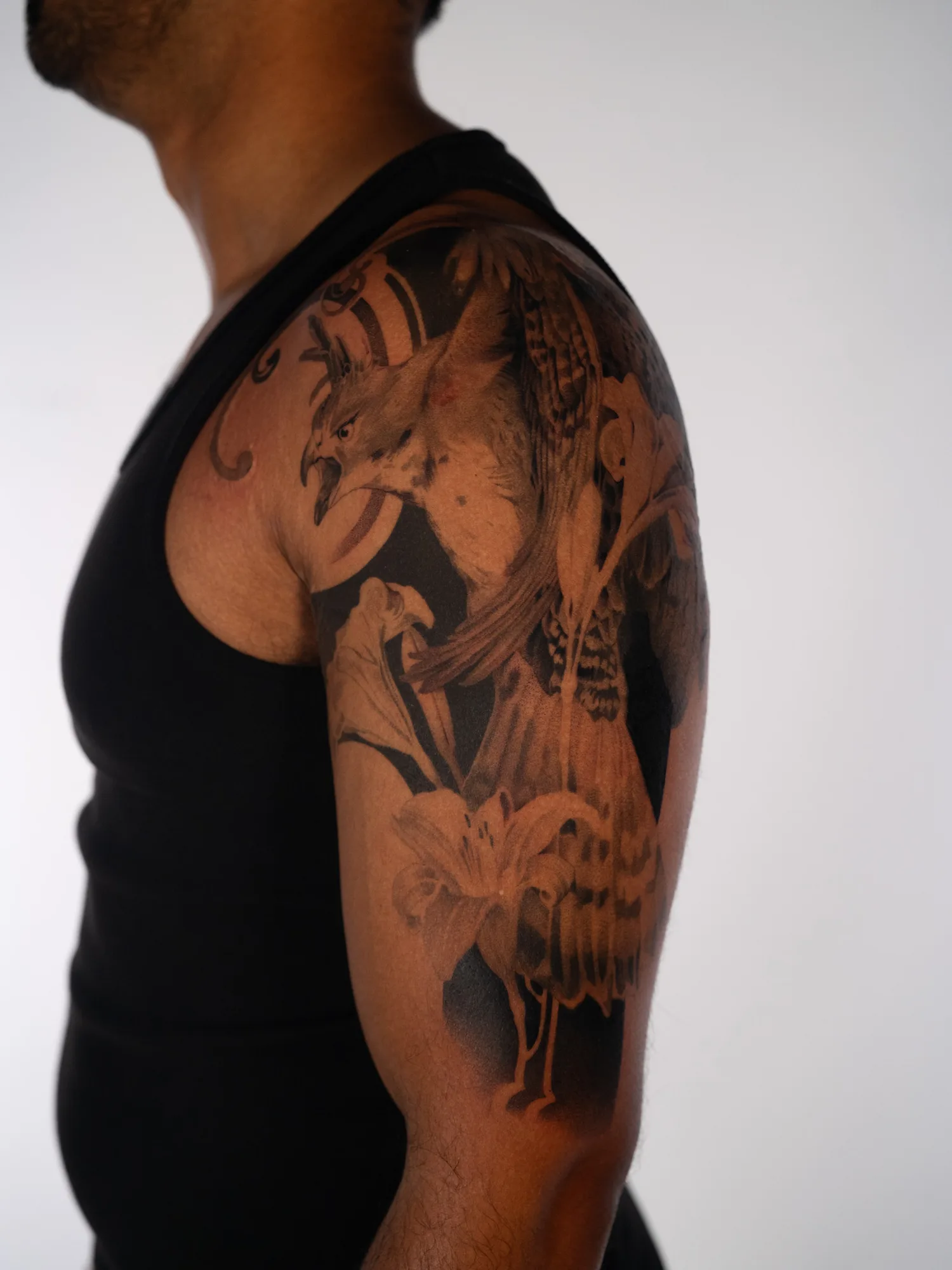 Black and grey realism half sleeve of a crested hawk eagle with lilies on a man's shoulder and upper arm.