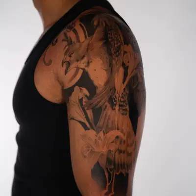 Black and grey realism half sleeve of a crested hawk eagle with lilies on a man's shoulder and upper arm.