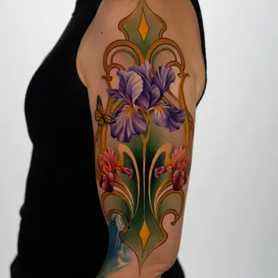 Color tattoo on the outer upper arm: a purple iris inside a gold and green Art Nouveau frame, with two red irises below and a small monarch butterfly on the left edge.