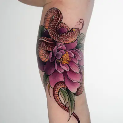 Color coverup tattoo on the upper arm: a red-scaled snake coiled through a large magenta peony with green leaves, its tail trailing toward the elbow.