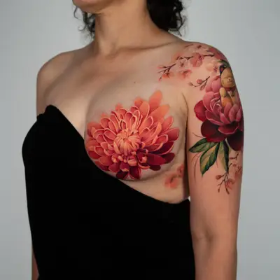 Color tattoo on the chest: a large orange and crimson chrysanthemum with a few sakura blossoms below it, beside a lucky cat and peony piece on the shoulder.