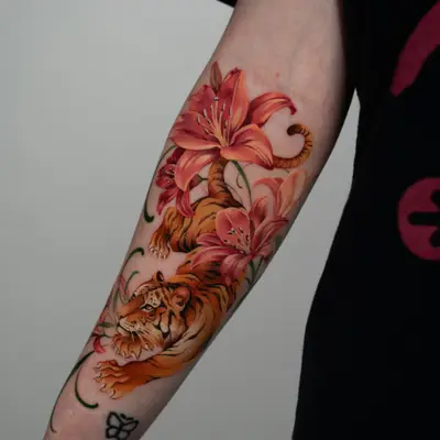 Color tattoo on the inner forearm: an orange tiger stalking downward through coral-pink tiger lilies with green stems, ending just above a small black butterfly tattoo at the wrist.